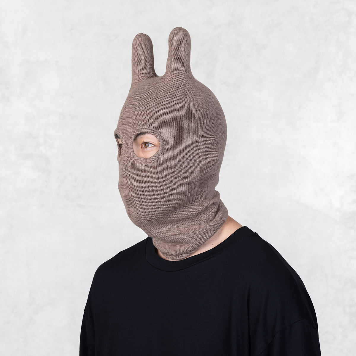 Person wearing a brown knit balaclava facing off to the side on a white background