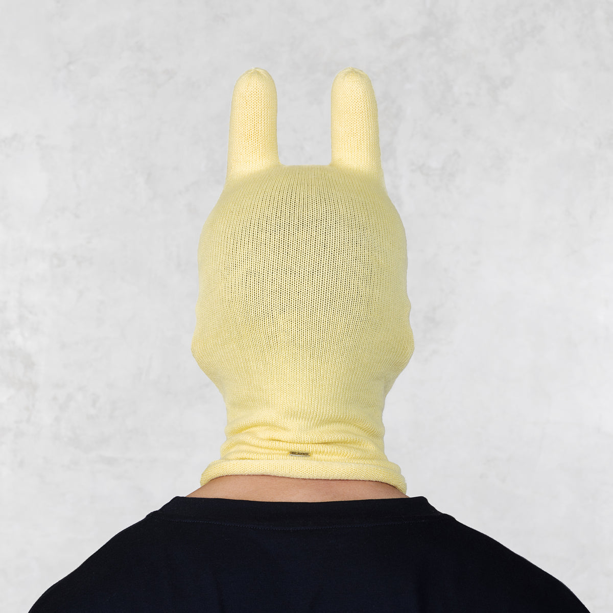 Person wearing a yellow knitted bunny mask with ears on a light gray background