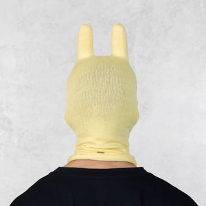Person wearing a yellow knitted bunny mask with ears on a light gray background