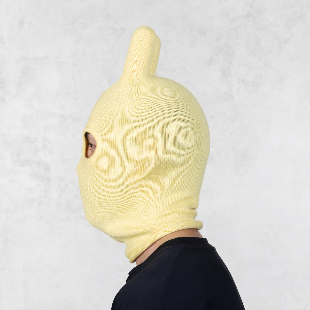 Person wearing a yellow knit mask on a light gray background