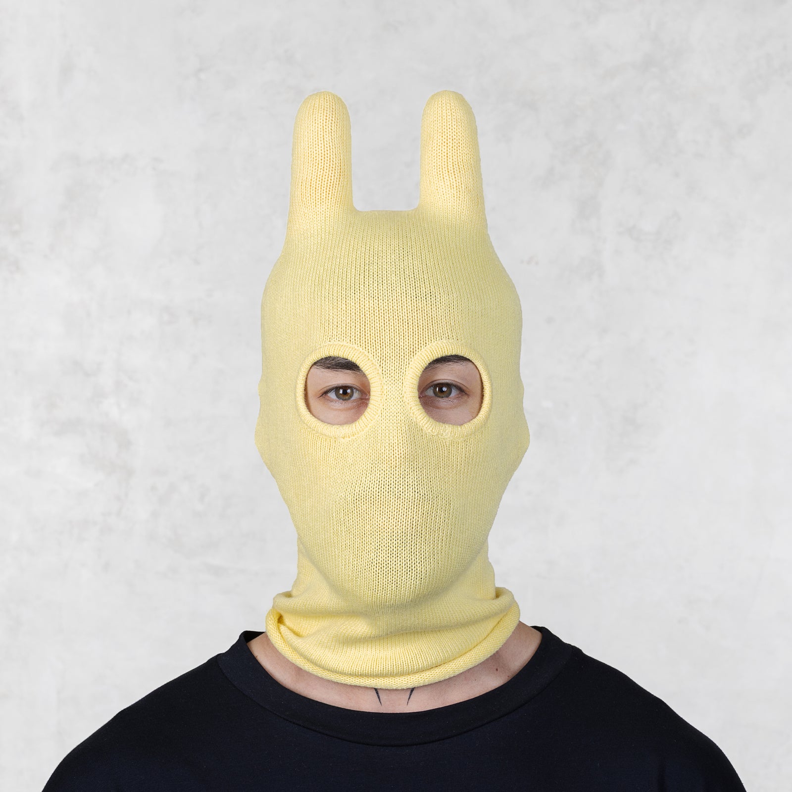 Person wearing a yellow bunny mask against a light gray background