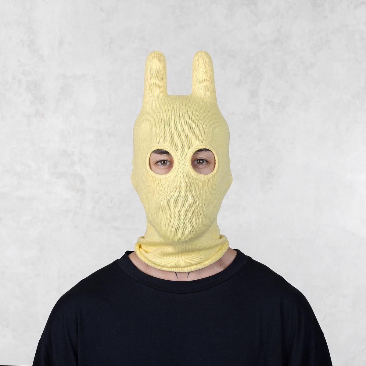 Person wearing a yellow bunny mask against a light gray background
