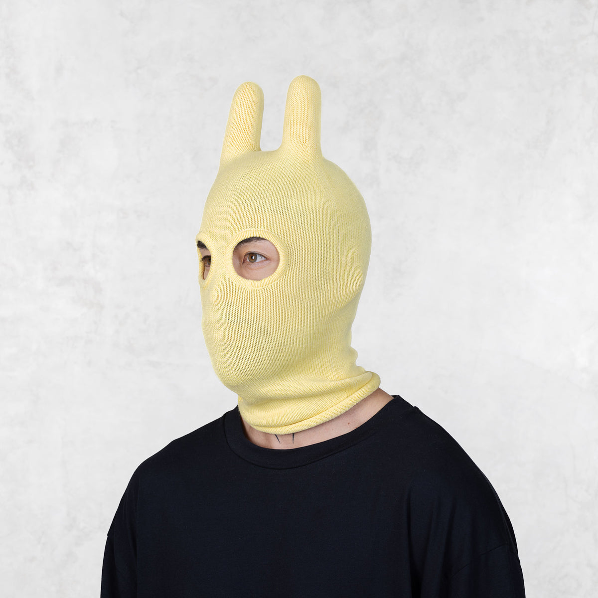 Person looking to the left wearing a yellow bunny mask against a white background