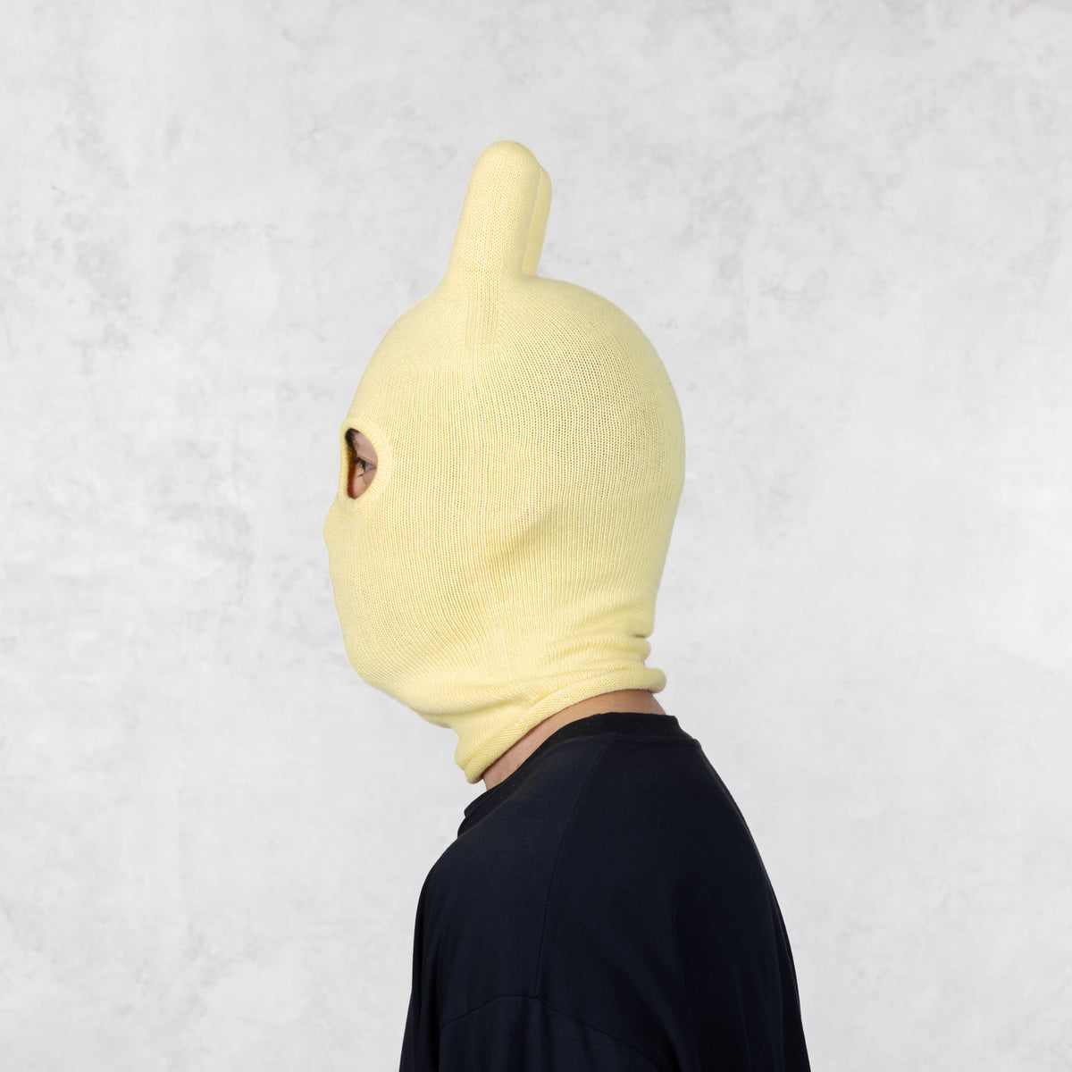 Side view of a person wearing a yellow bunny mask on a light gray background