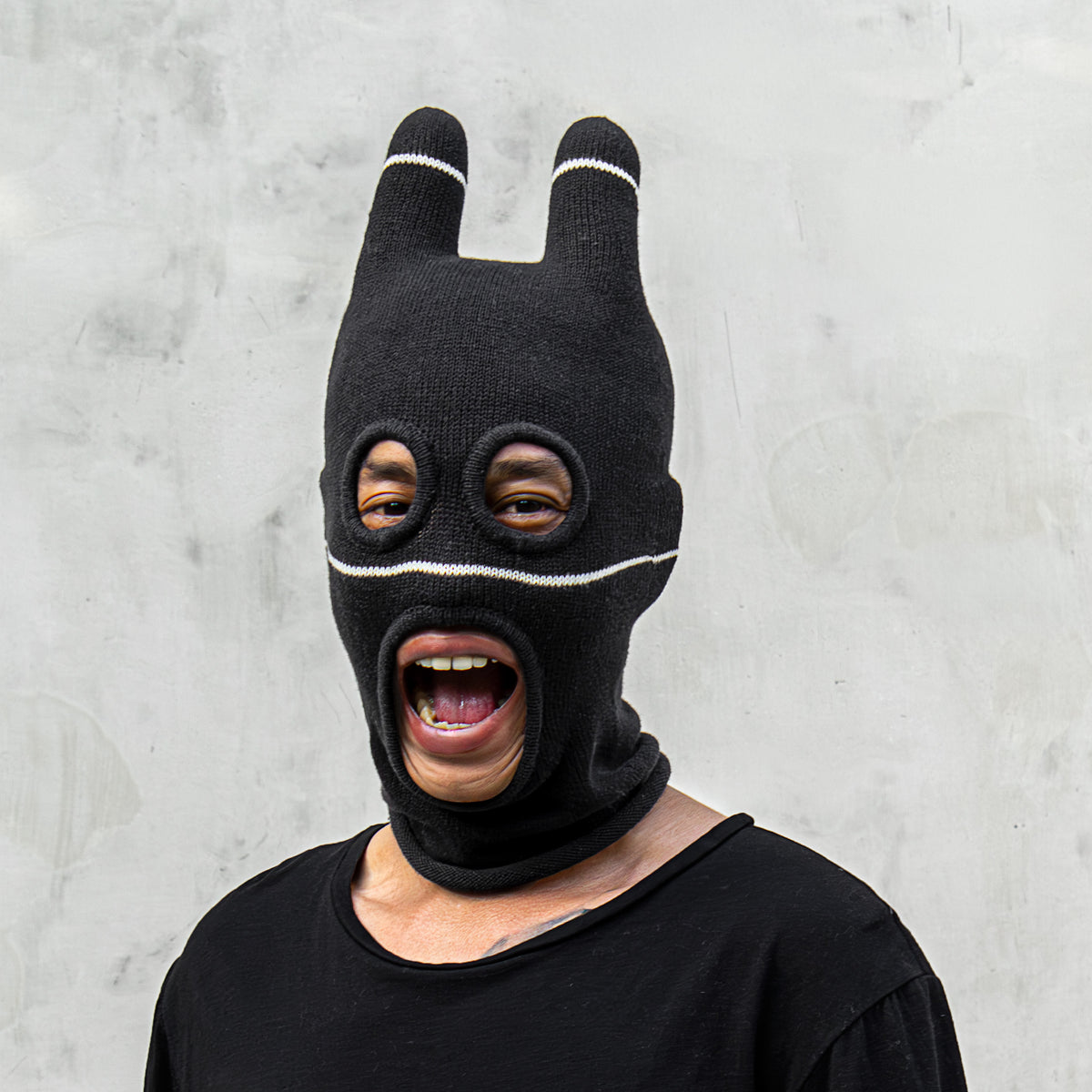 Person with their mouth open wearing a black balaclava with ears against a gray background 