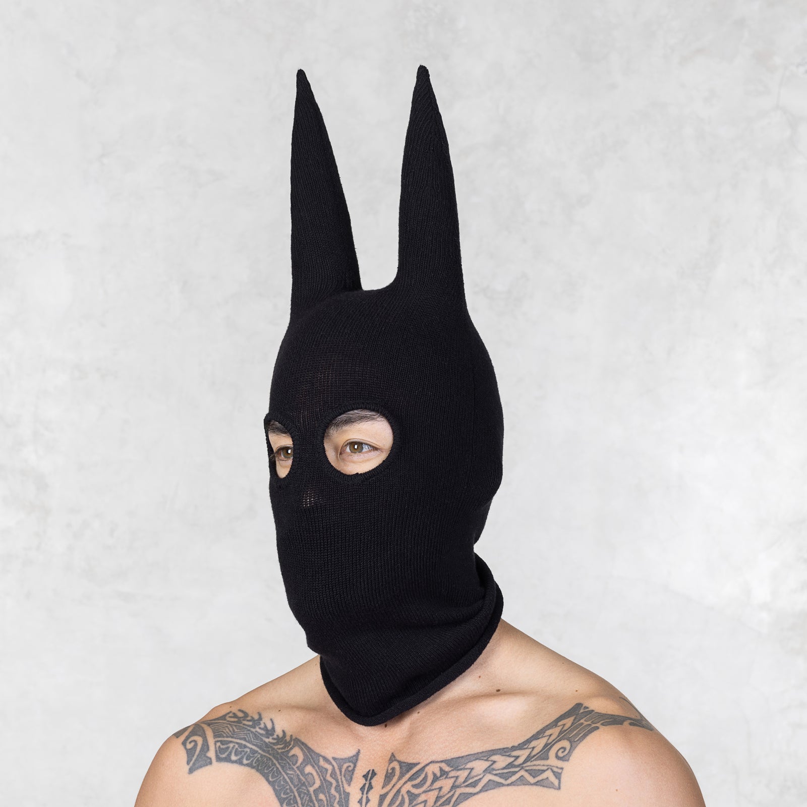 Person wearing a black knitted mask with long horns against a light gray background