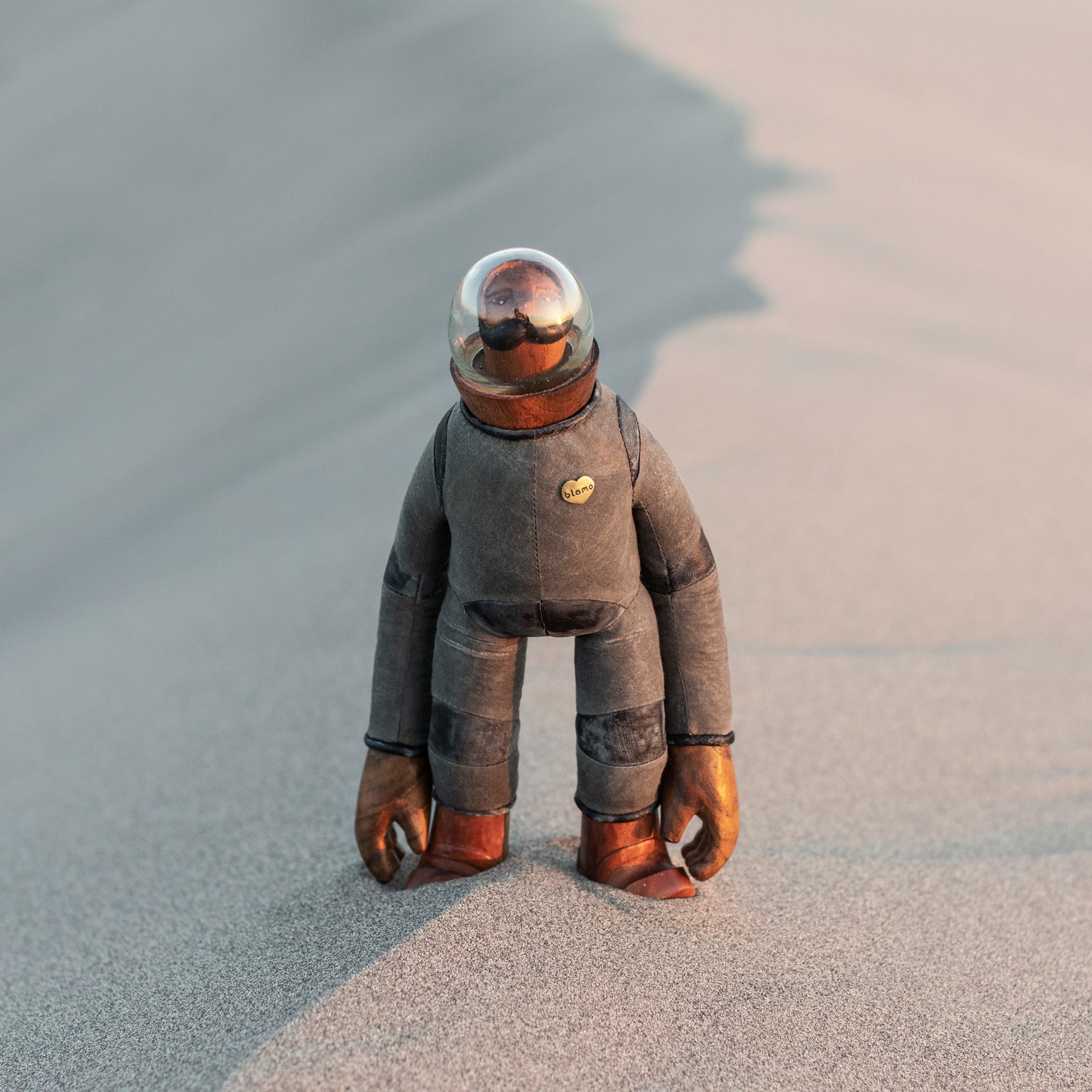 Wooden and leather astronaut figurine with a mustache and a glass globe over the head standing in the sand