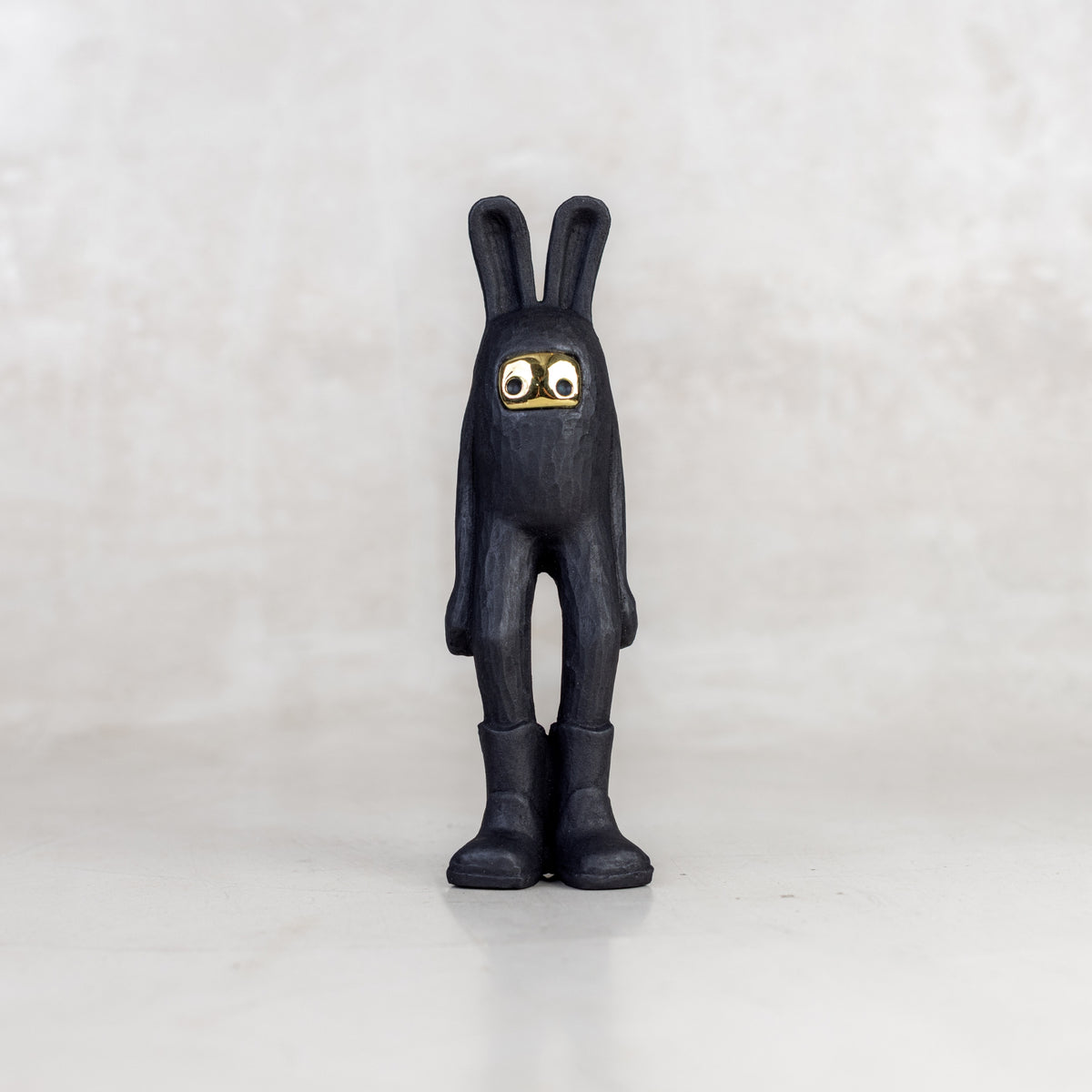 A black rabbit-like figurine  with a brass mask face on a white background