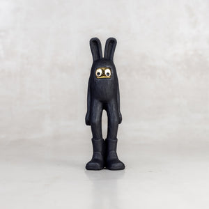 A black rabbit-like figurine  with a brass mask face on a white background