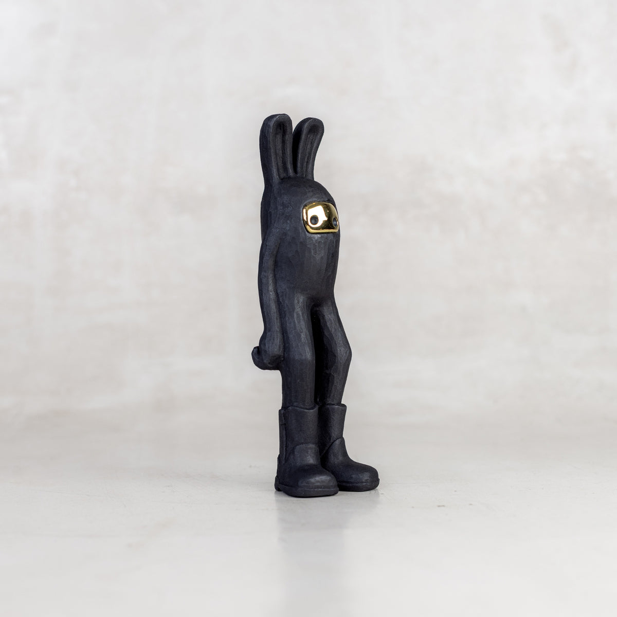 Quarter view of a black rabbit-like figurine with a brass mask face on a white background