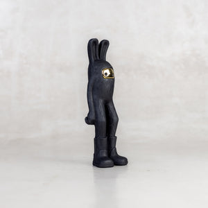 Quarter view of a black rabbit-like figurine with a brass mask face on a white background