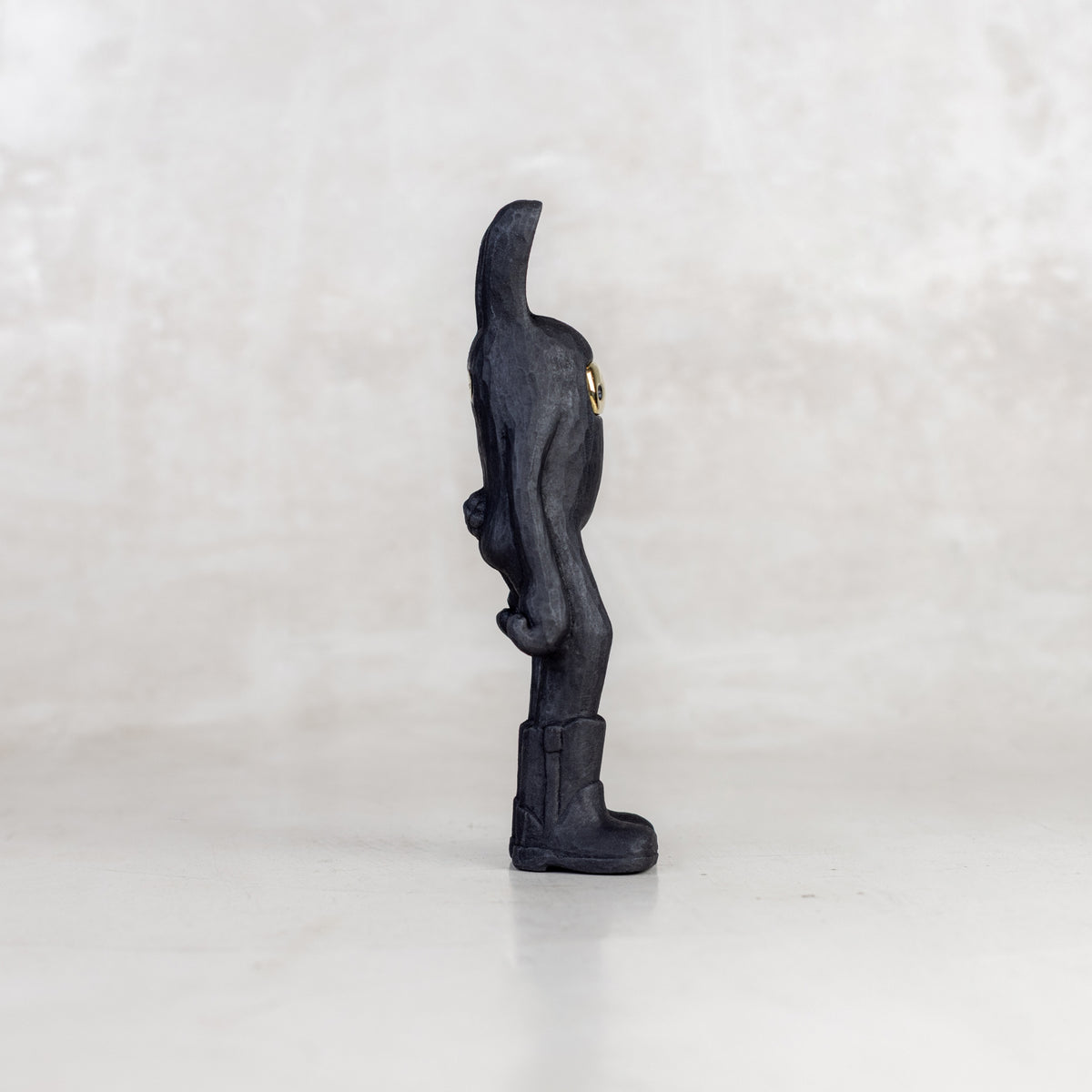 Side view of a black rabbit-like figurine with a brass mask face on a white background