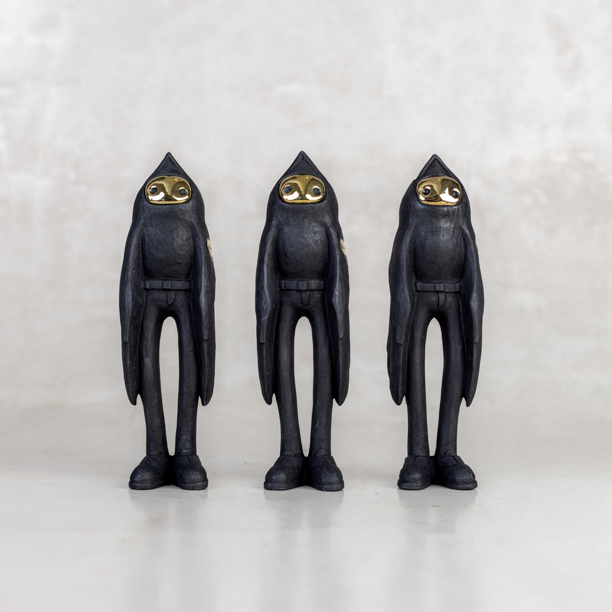 Three black birdman figurines with brass gold faces on a white background