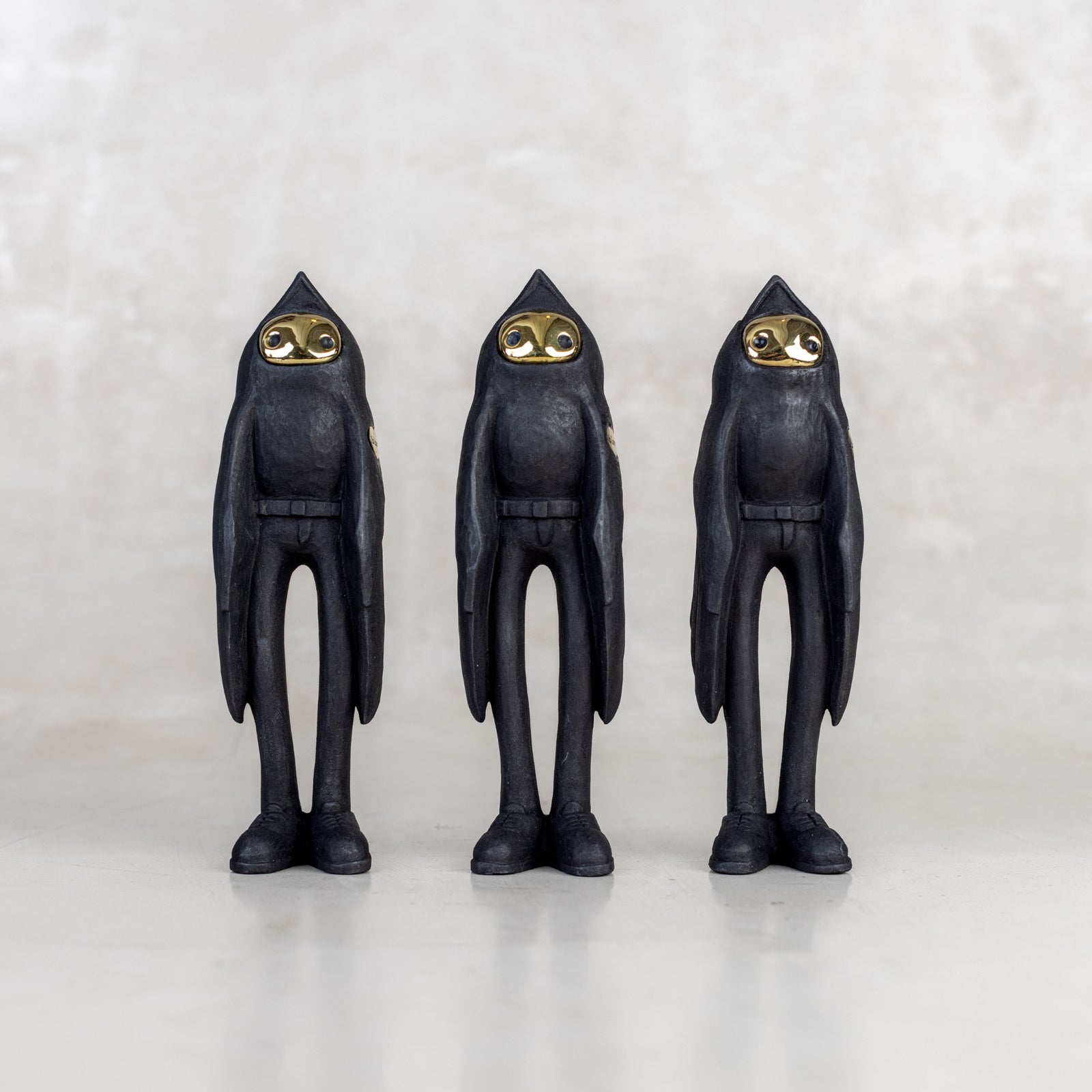 Three black birdman figurines with brass gold faces on a white background