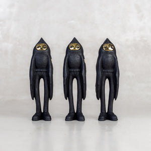 Three black birdman figurines with brass gold faces on a white background