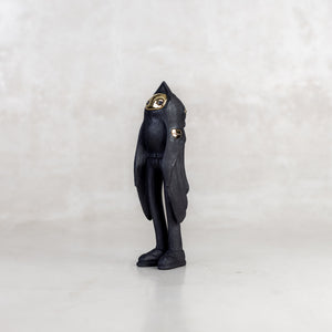 Quarter view of a black birdman figurine with a brass gold face on a white background