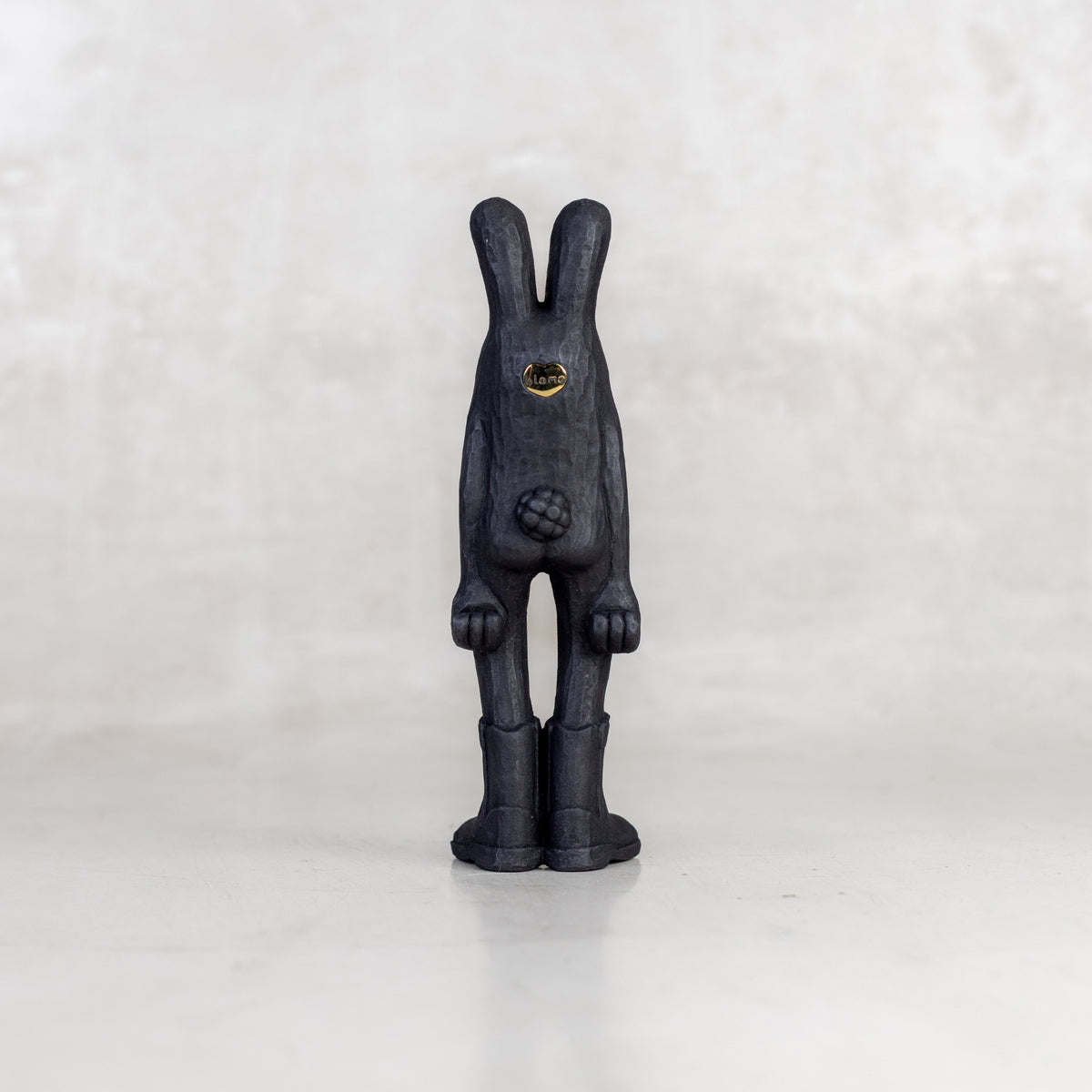 Black view of a black rabbit-like figurine with a brass emblem on a white background