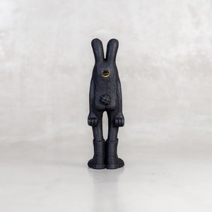 Black view of a black rabbit-like figurine with a brass emblem on a white background