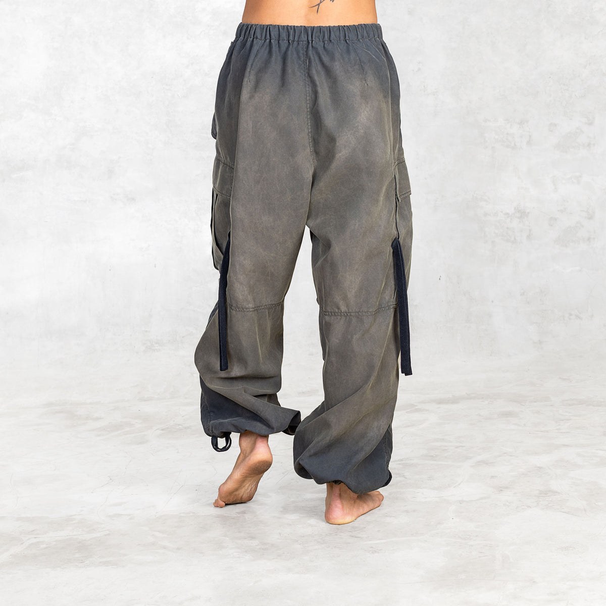Back view of person wearing hand painted olive oversized parachute pants on a white background