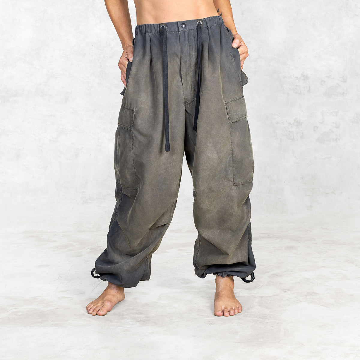 Person from front view wearing hand painted olive oversized parachute pants on a white background with hands in pockets