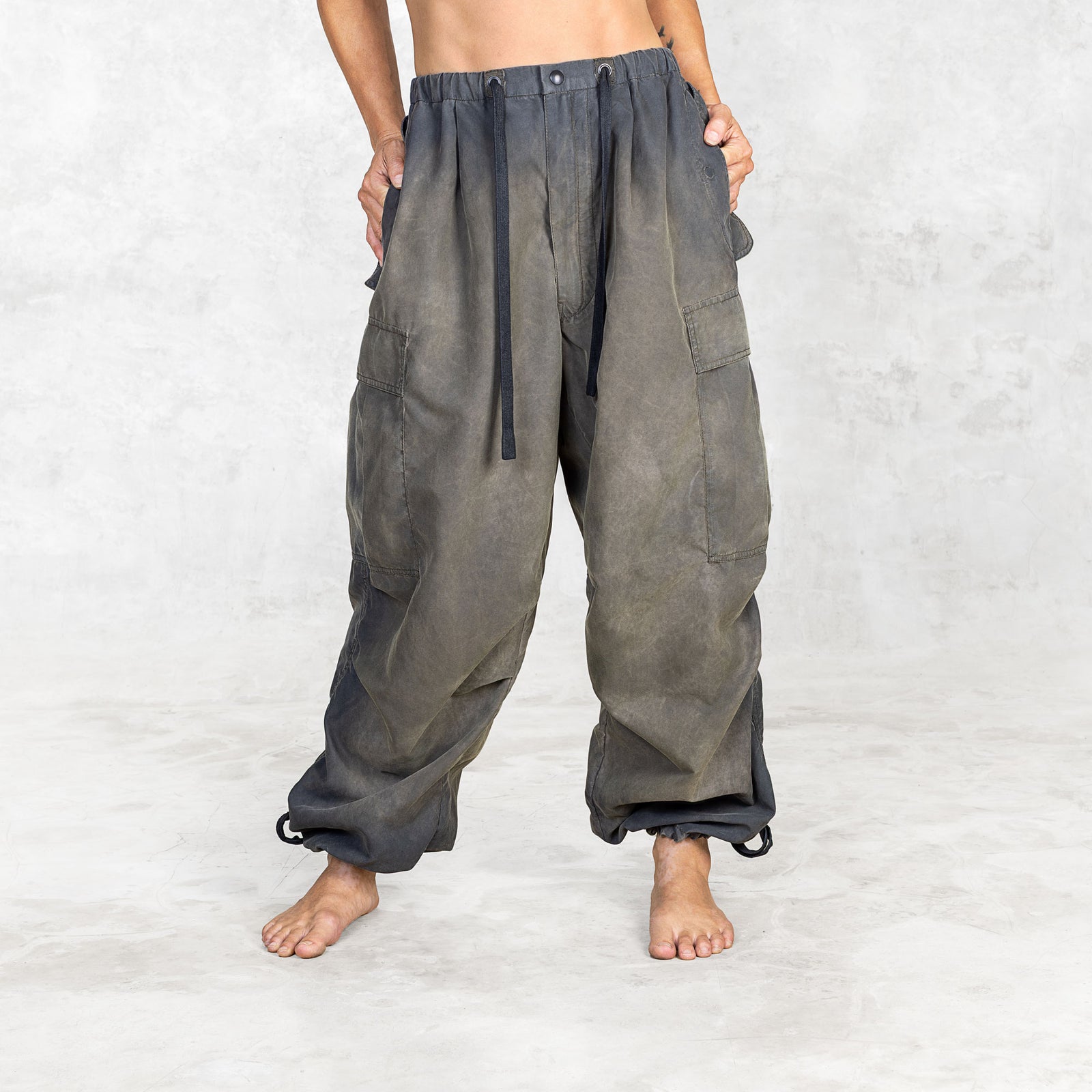 Person from front view wearing hand painted olive oversized parachute pants on a white background with hands in pockets