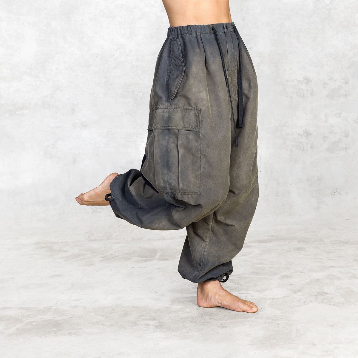 Person wearing hand painted olive oversized parachute pants on a white background with kicked leg