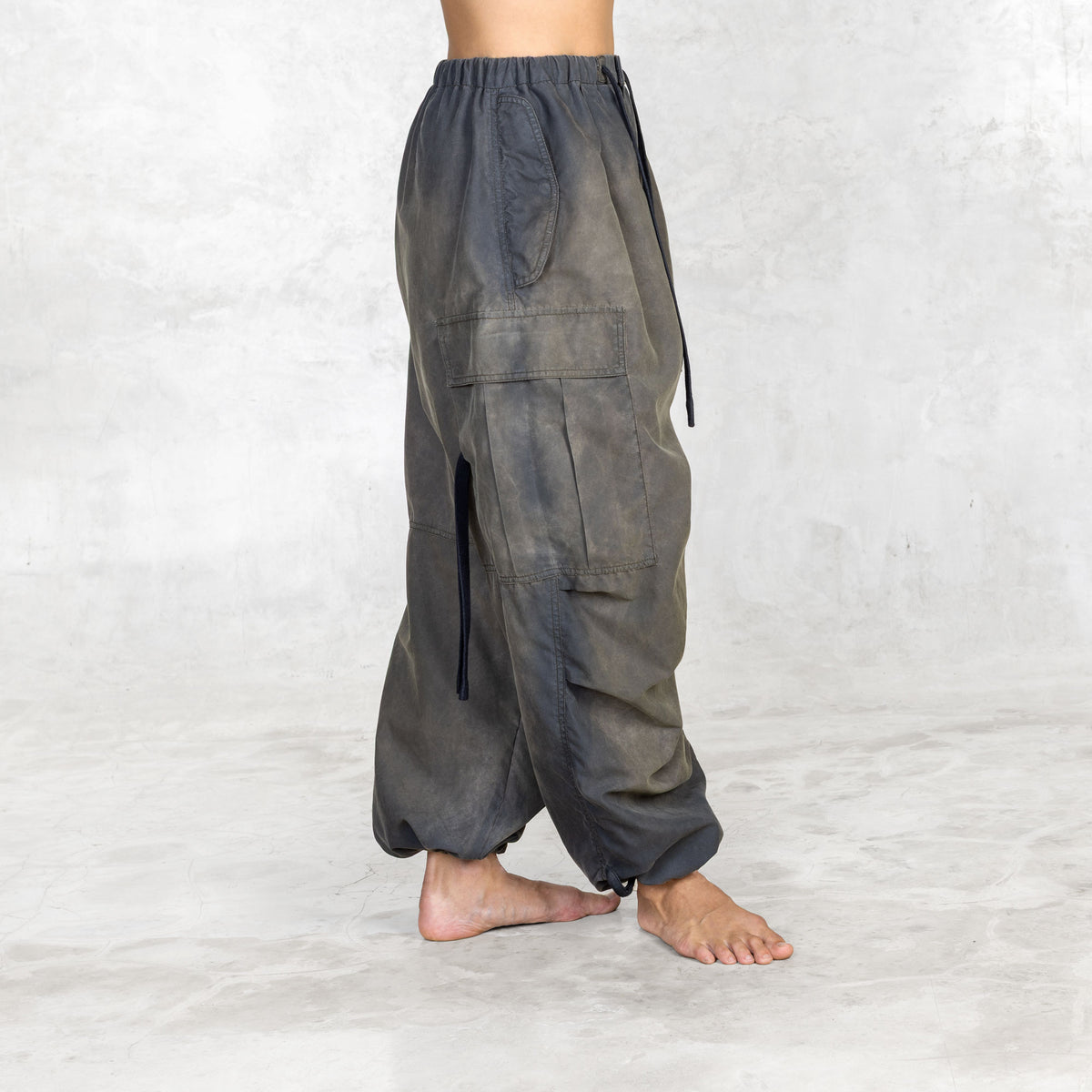 Side view of person wearing hand painted olive oversized parachute pants on a white background