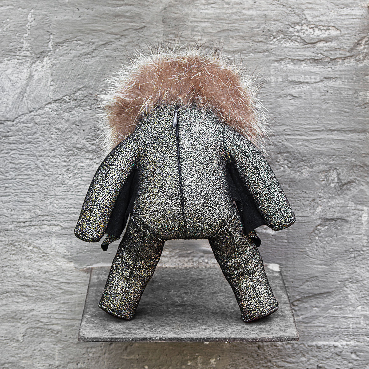 Back view of a sparkly leather stuffed toy with a brass head and fur on a gray background