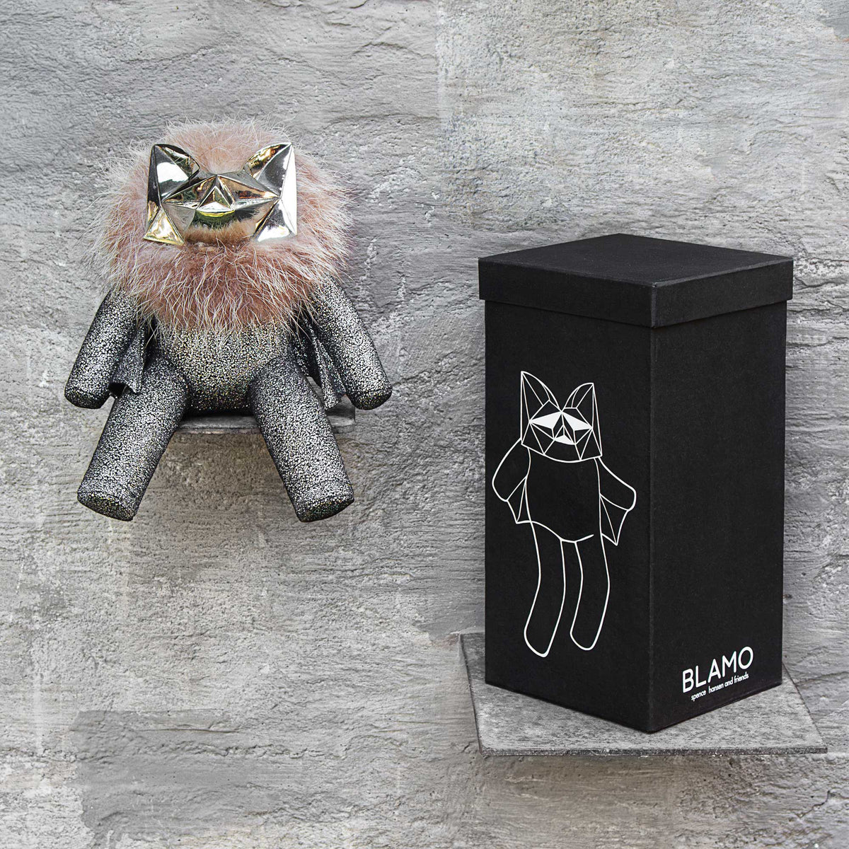 Sparkly leather stuffed toy with a brass head and fur sitting with its box on a gray background