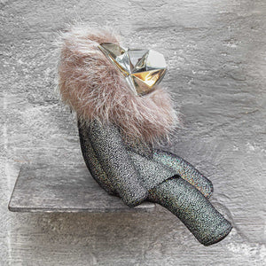 Side view of a sparkly leather stuffed toy with a brass head and fur on a gray background