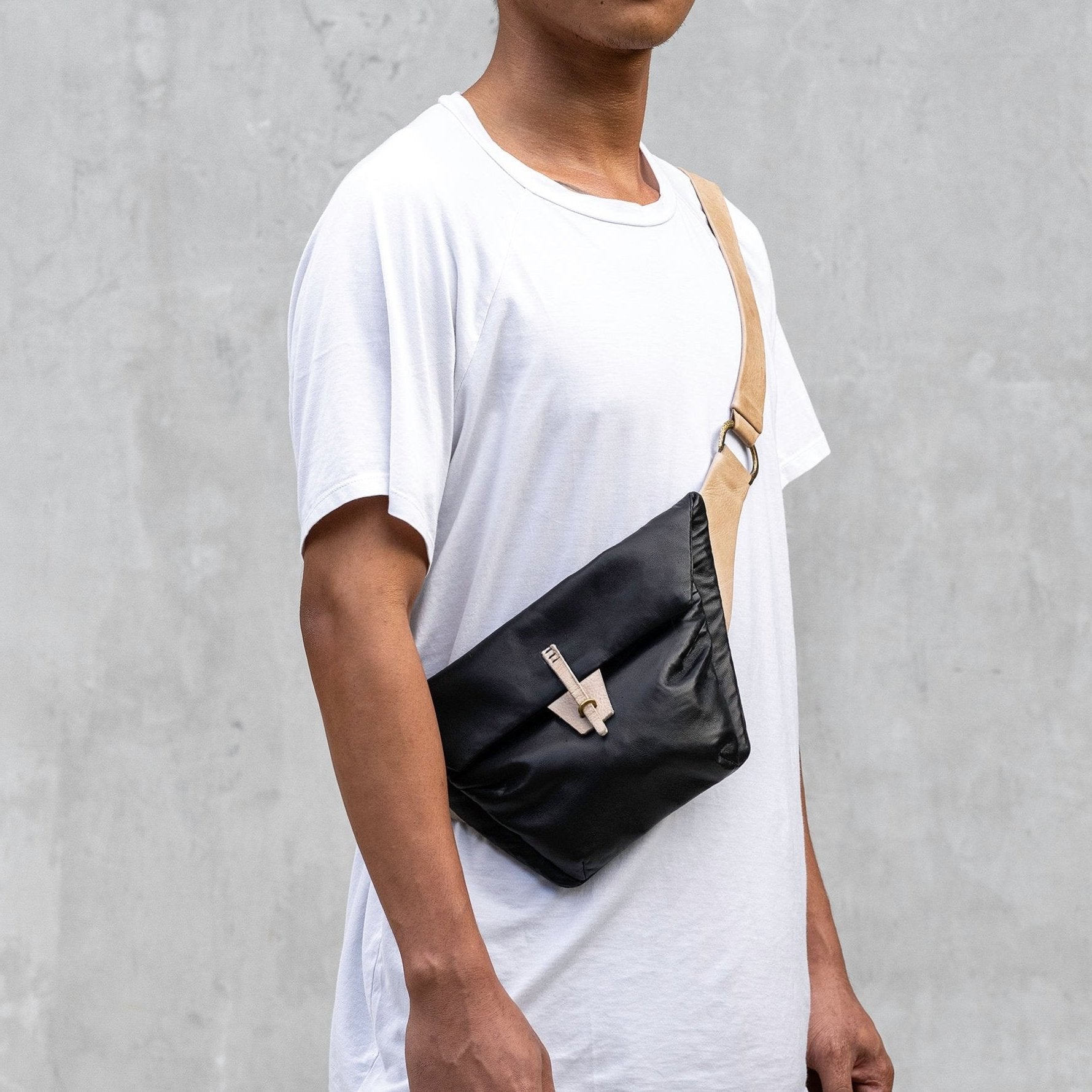 A man dressed in a white t-shirt and a black belt bag, standing confidently against a neutral background.