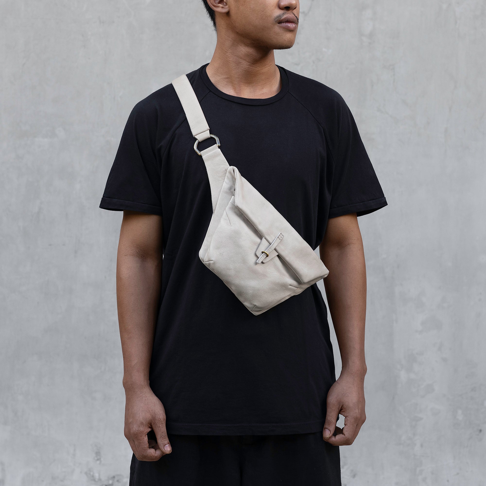 A man dressed in a black shirt, accessorized with a cool white leather belt bag, stands confidently against a neutral background.