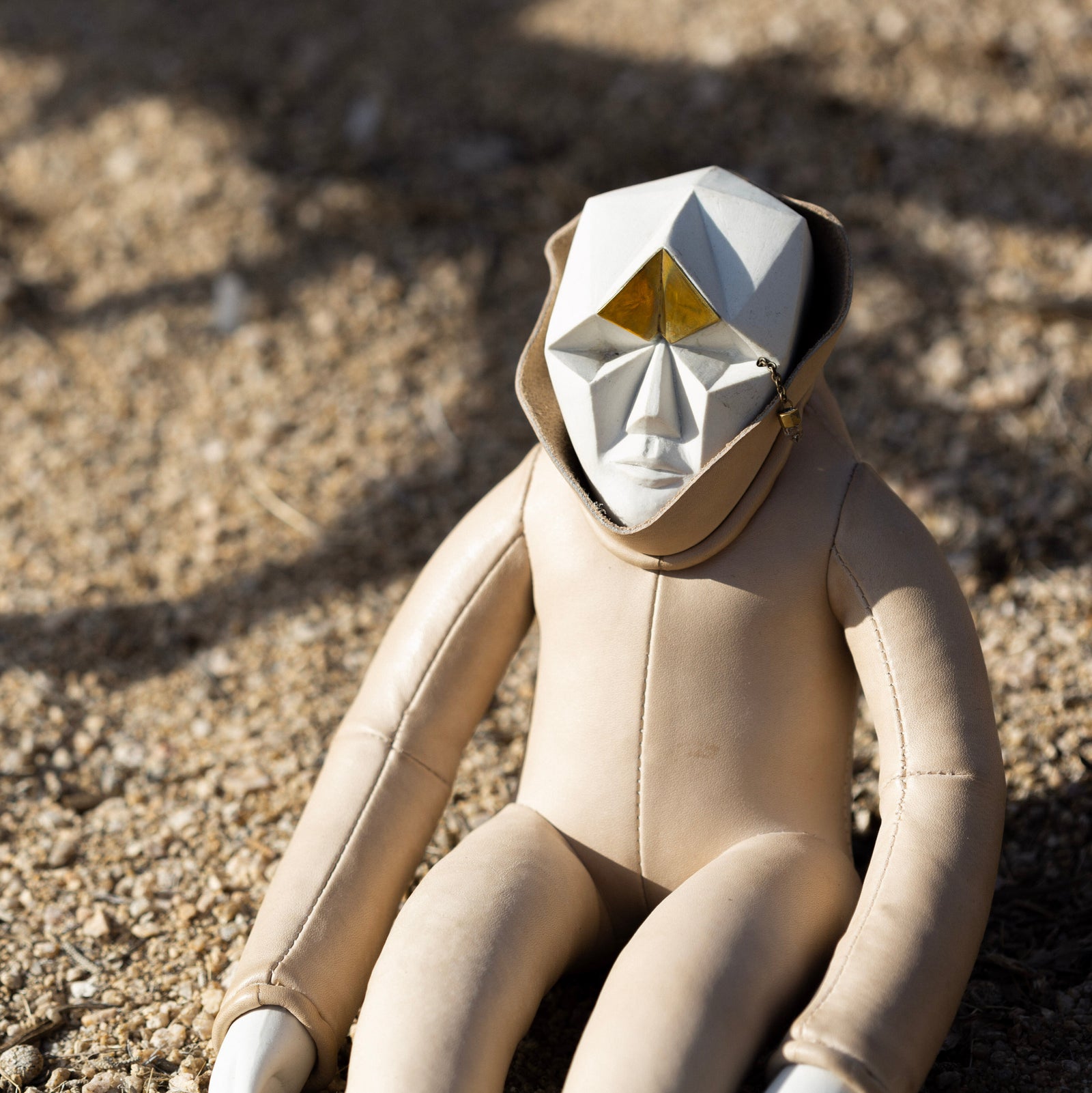 Ceramic, brass, and leather figurine with a geometric face sitting on a rocky surface