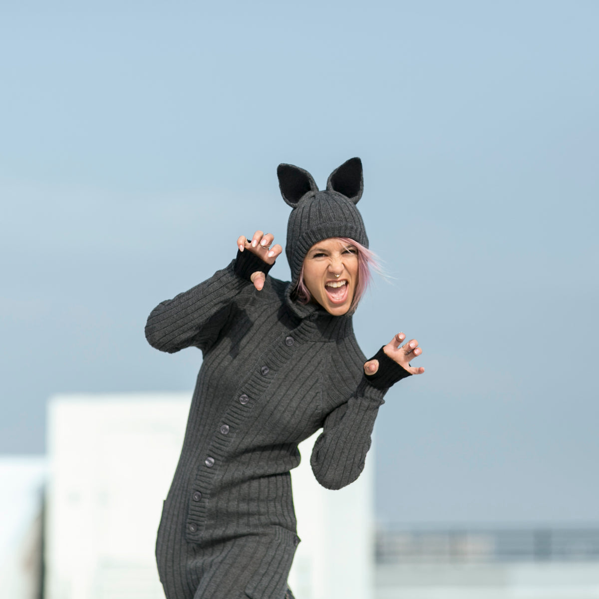 person wearing a wolf onesie with their mouth open and hands shaped like claws with a clear sky in the background
