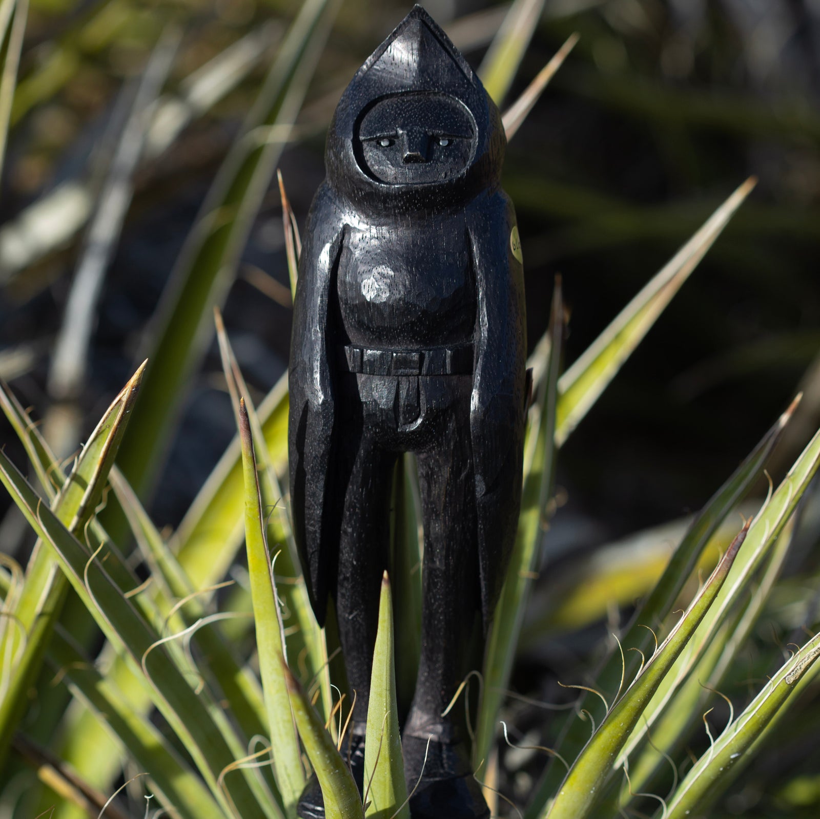 Black wooden sculpture of a raven in a natural setting standing in a green plant