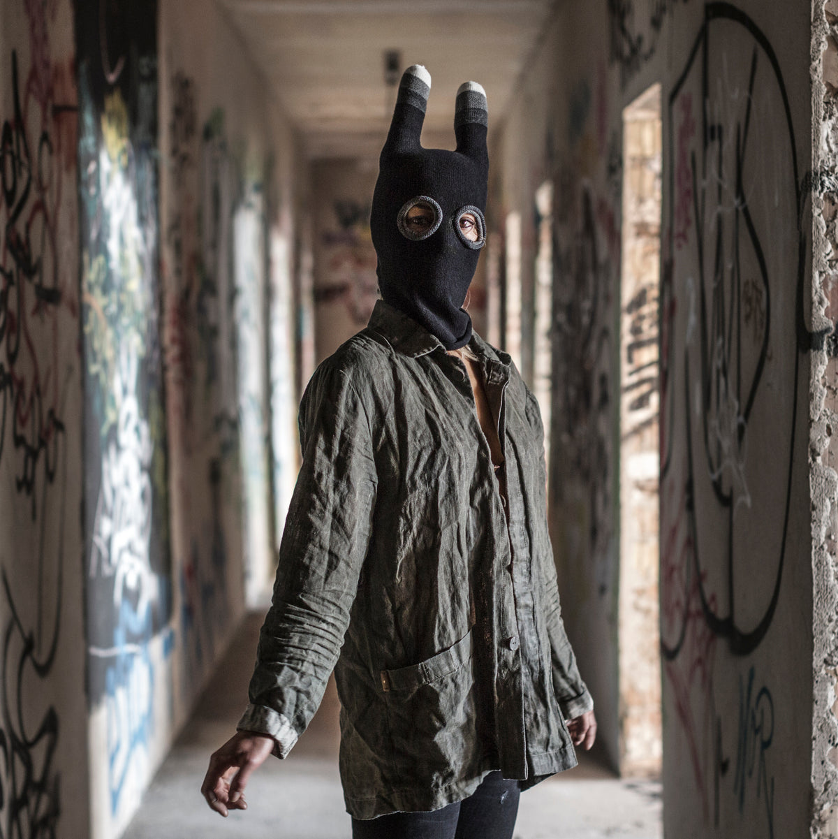 Person wearing a mask with ears standing in a hallway with graffiti on the walls