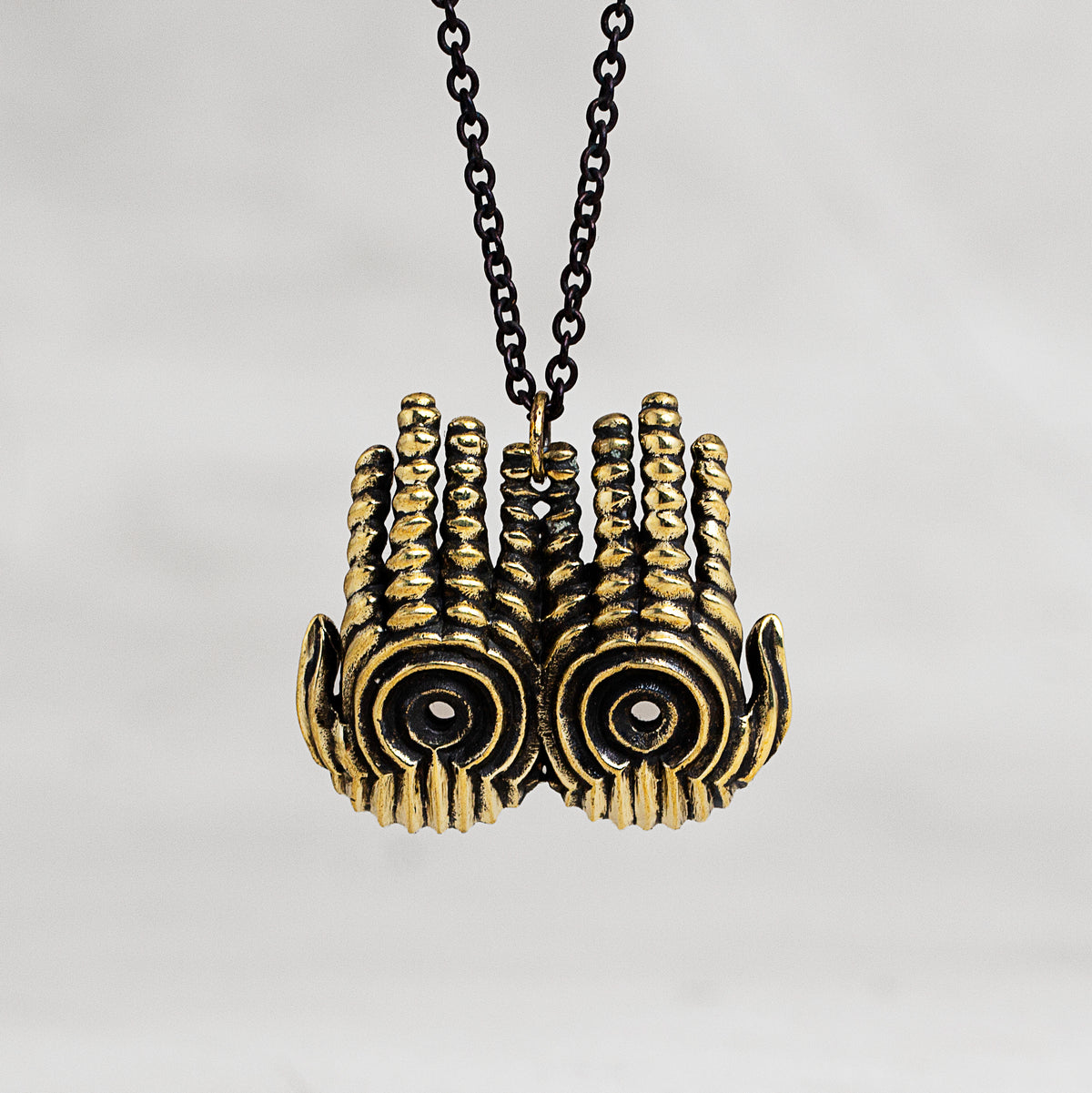 A gold-toned hand pendant necklace with a black chain, shown against a neutral light gray background.
