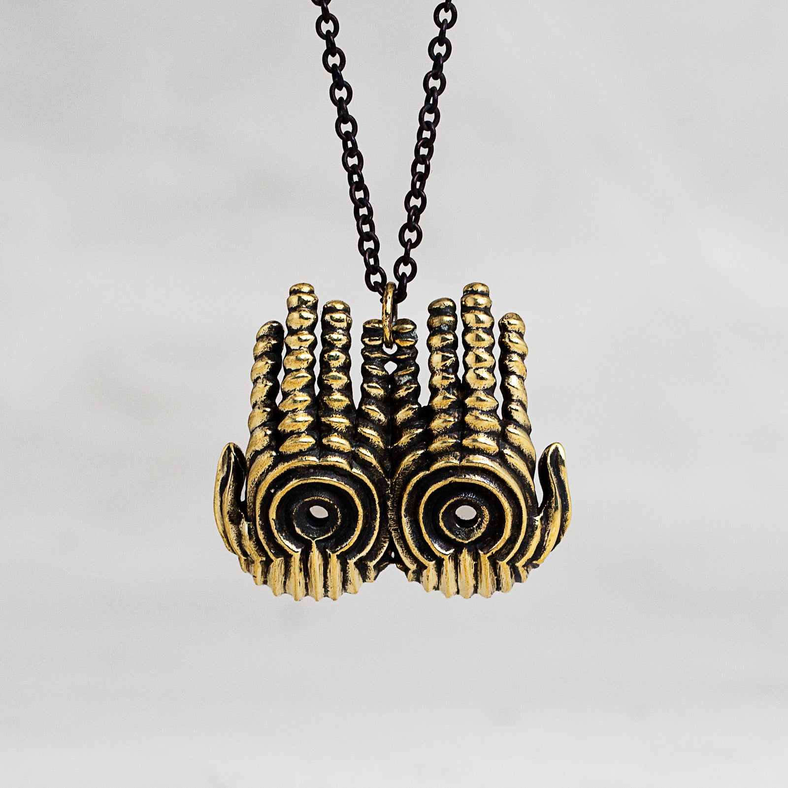 A gold-toned hand pendant necklace with a black chain, shown against a neutral light gray background.