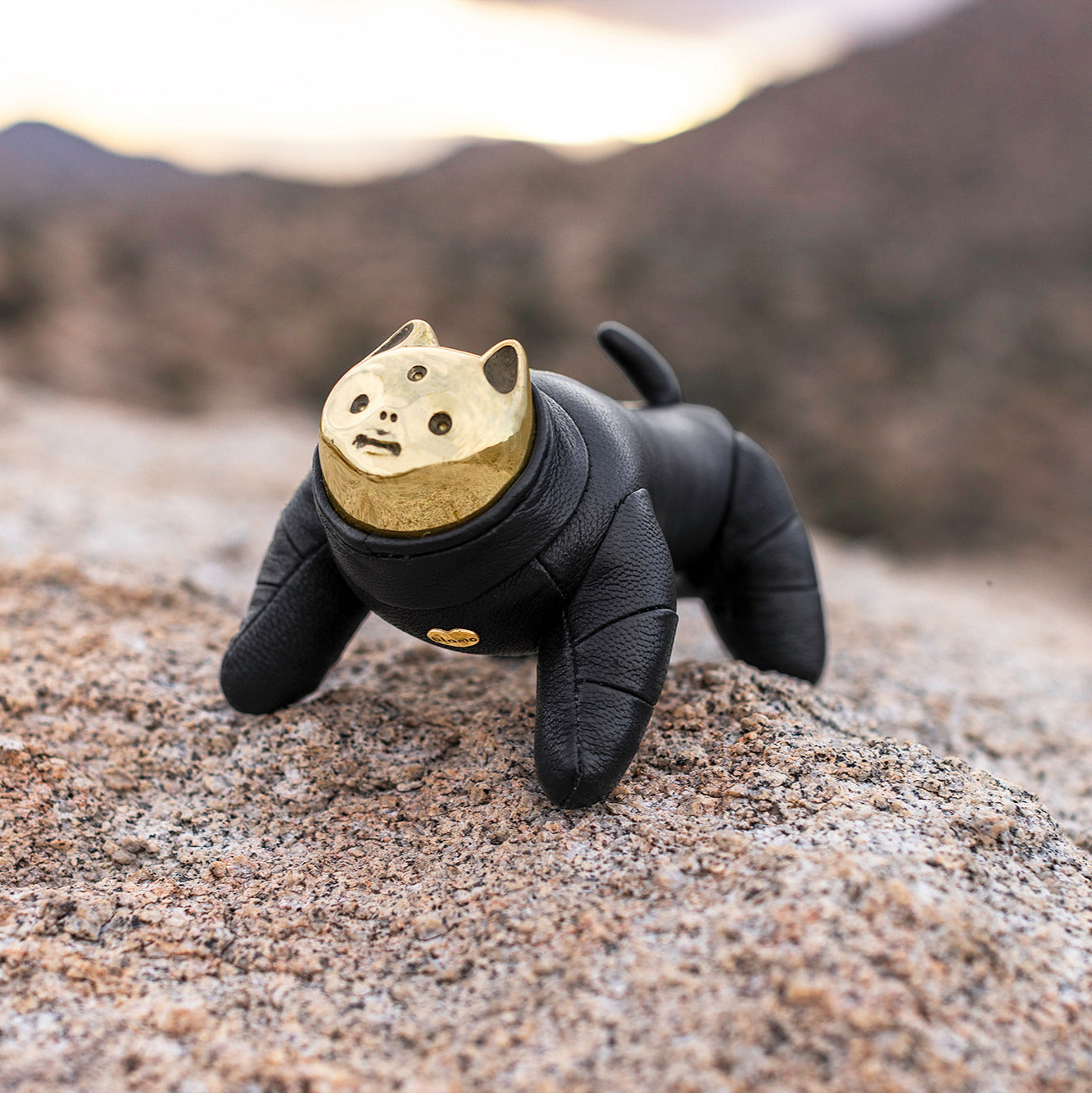 Black and gold figurine resembling a cat on a rocky surface with a blurred natural background