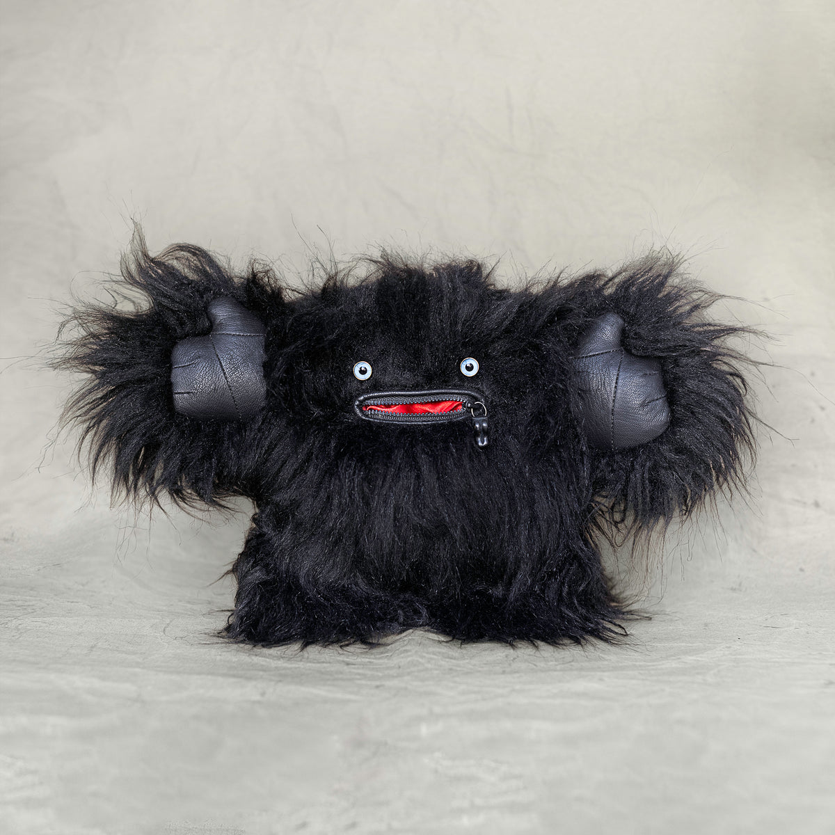 Black furry creature plush toy on a light gray background