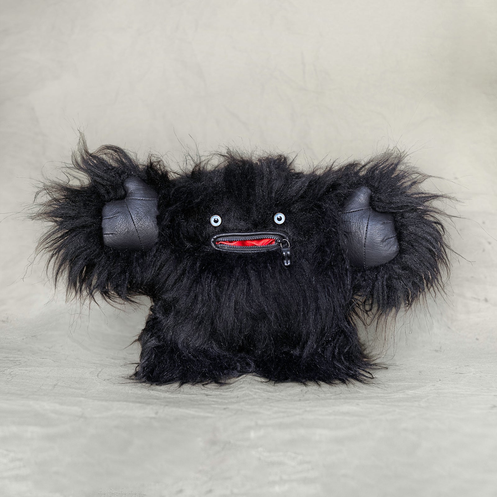 Black furry creature plush toy on a light gray background