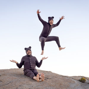 Two people in bear costumes in different poses on a rock with clear skies