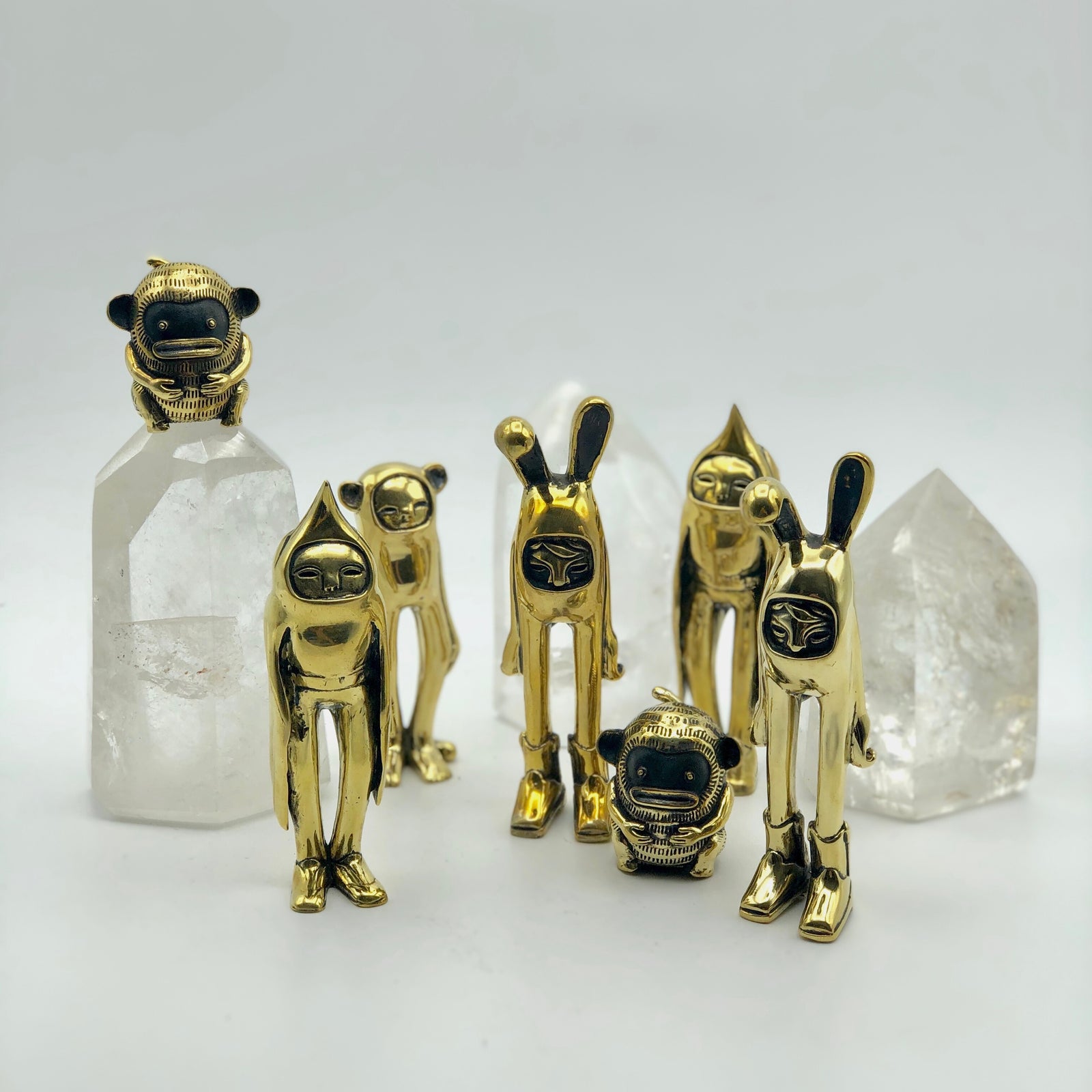 Brass bunny rabbit, bird, and monkey figurines standing in a group with crystals on a white surface 