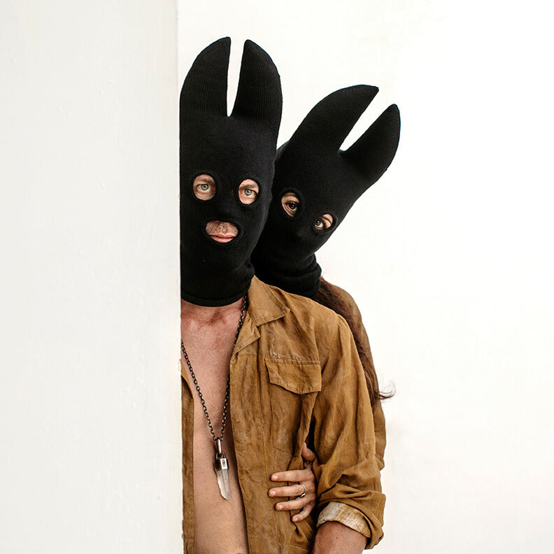 Two people wearing black bat masks peeking from behind a white panel.