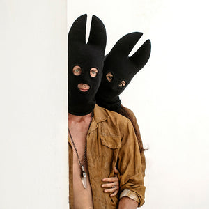 Two people wearing black bat masks peeking from behind a white panel.
