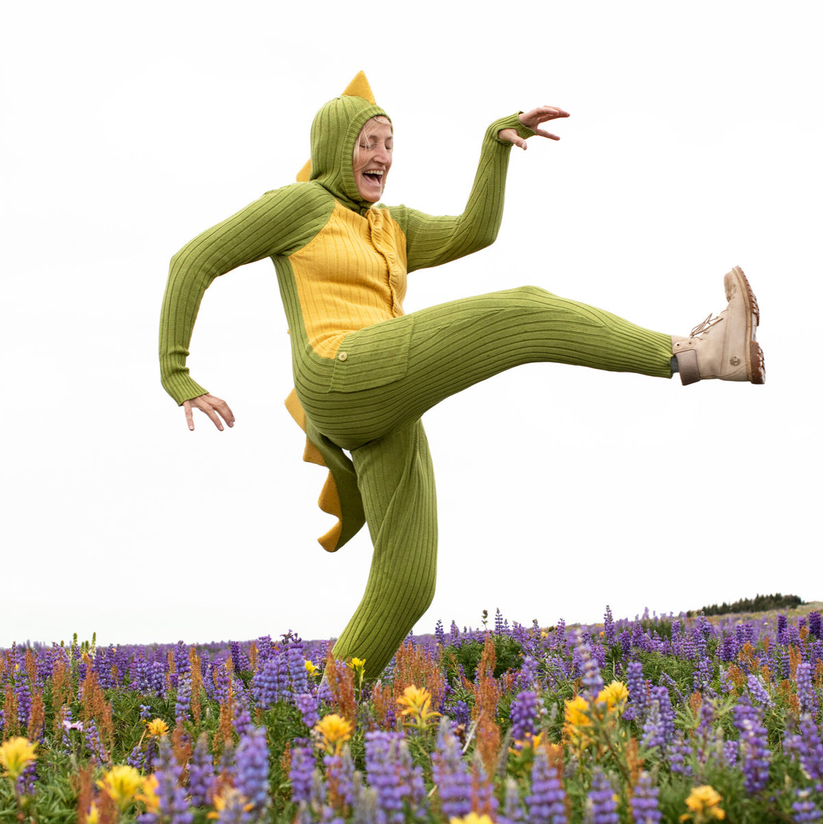 Person in a green and yellow onesie jumping in a field of flowers