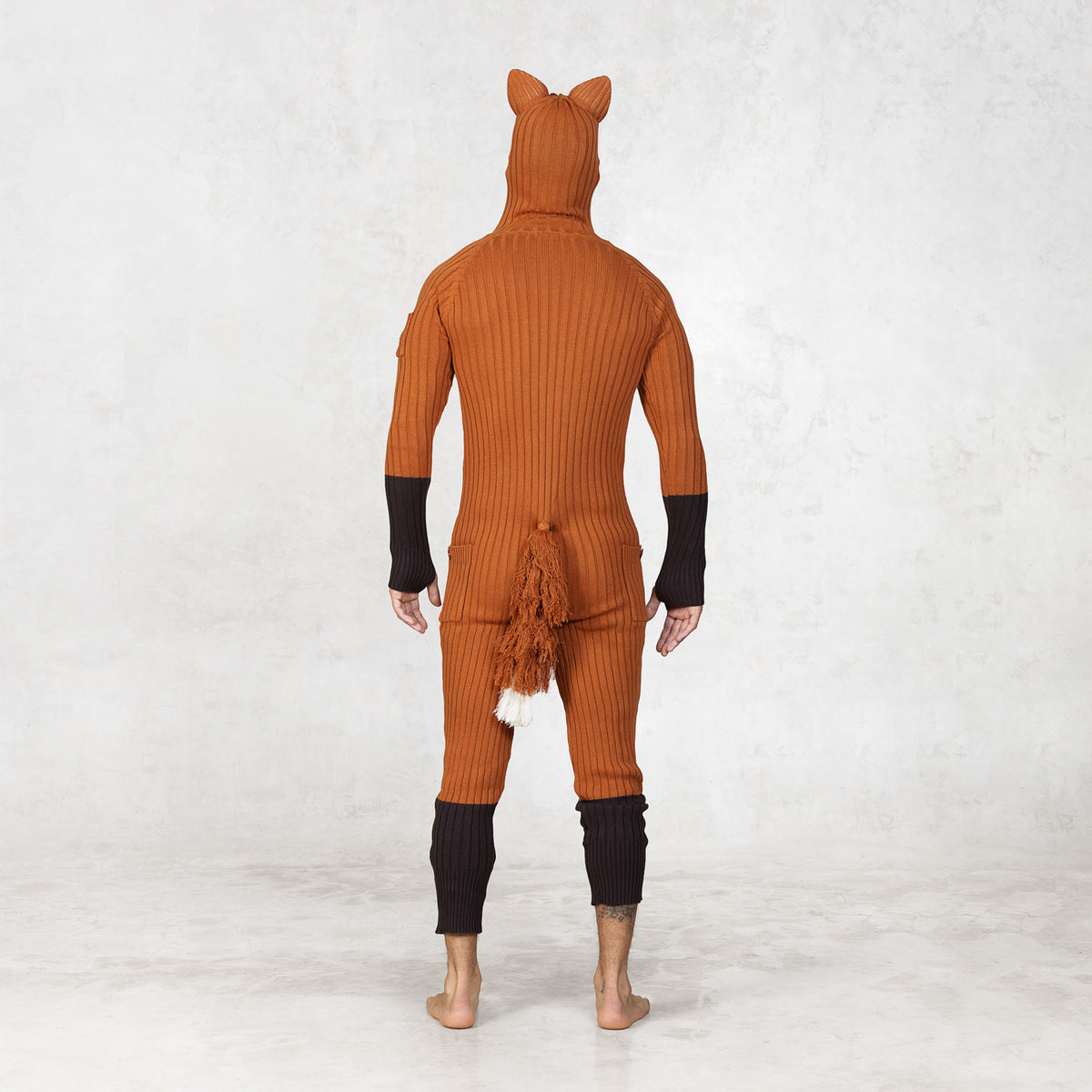 Person wearing a fox-themed onesie with a hood facing backwards on a white background