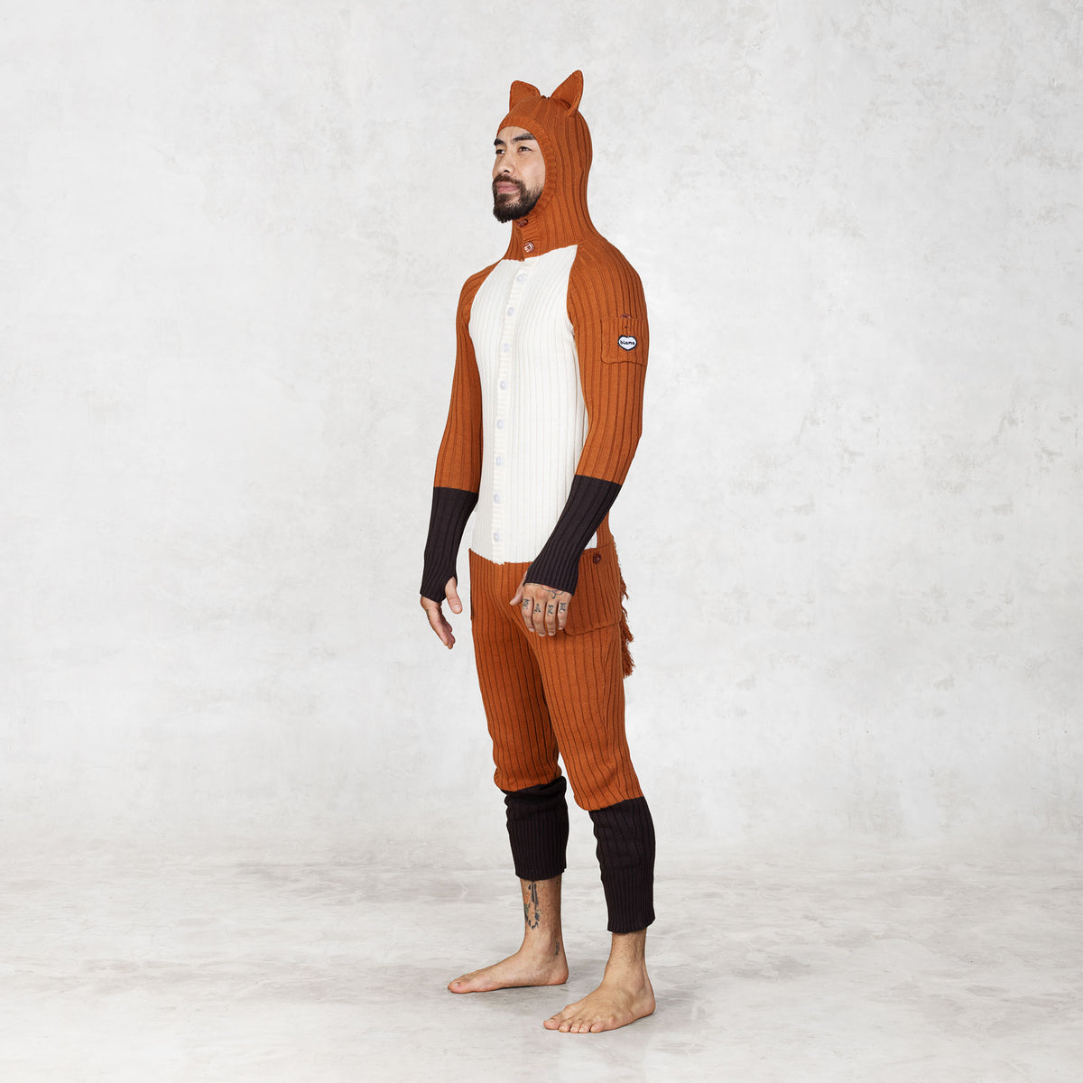 Person wearing a fox-themed onesie looking off to the side with a hood on a white background