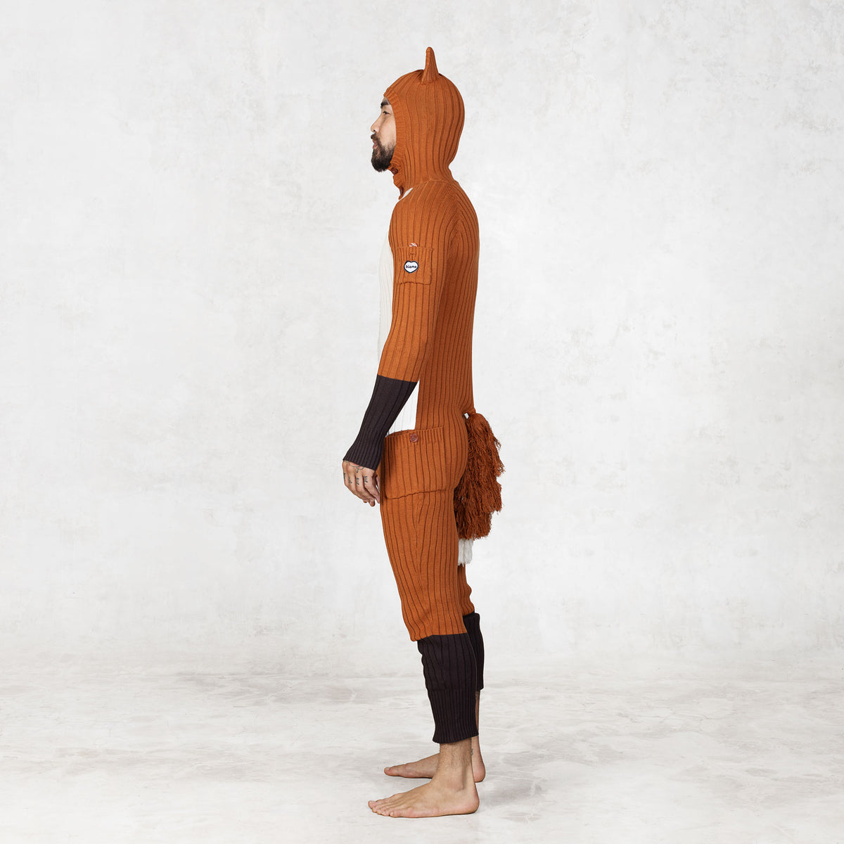 Person wearing a fox-themed onesie with a hood facing sideways on a white background