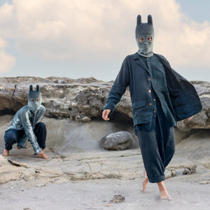 Two people wearing animal masks on a rocky landscape with a cloudy sky.